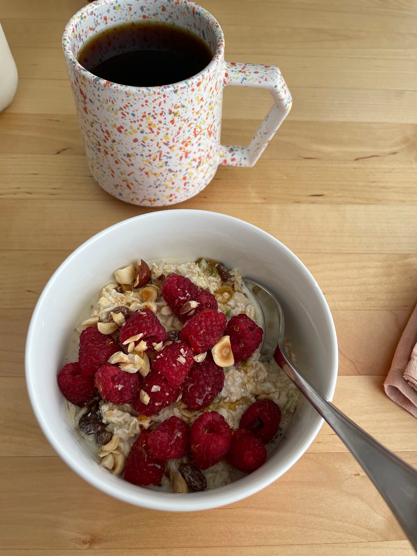 A bowl of bircher muesli topped with raspberries and hazelnuts, a coffee cup in the background.