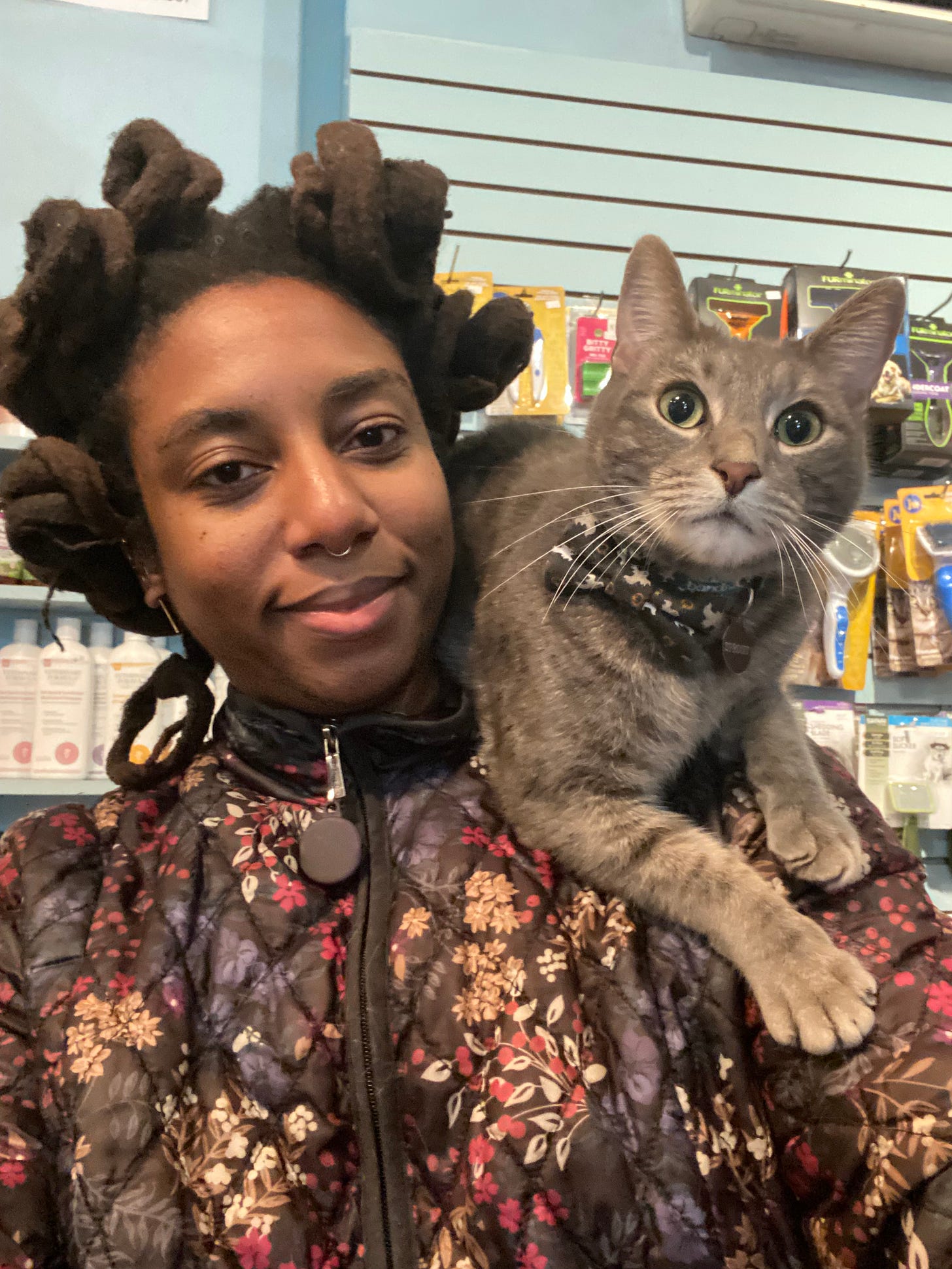 N3VLYNNN smiles contentedly with a cat calmly sitting on her shoulder in a pet shop