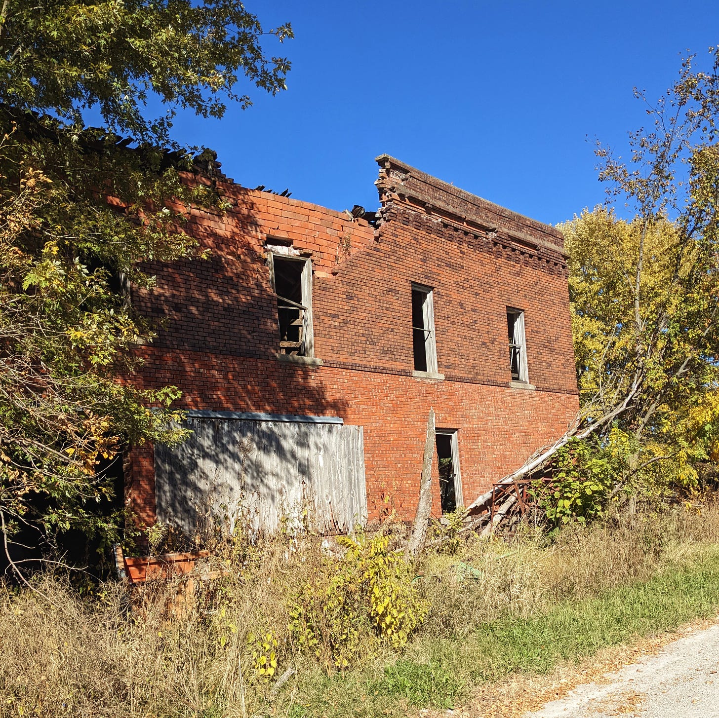 An abandoned brick building missing its roof and windows, surrounded by trees