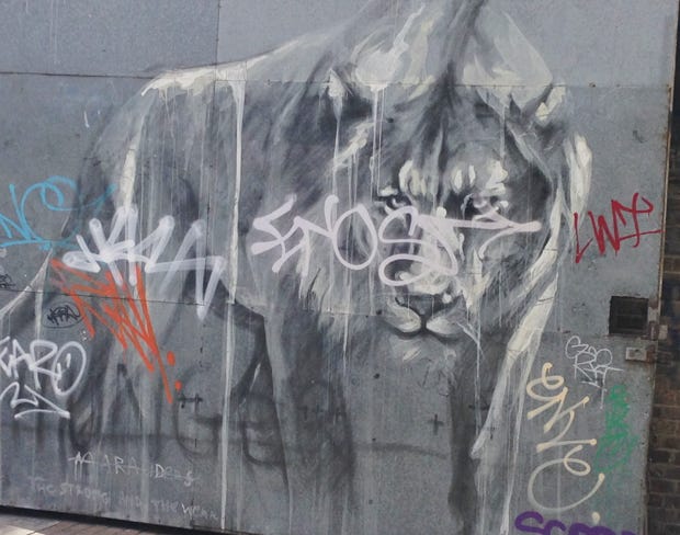 Street mural of a lion in grays and white with graffiti words over it