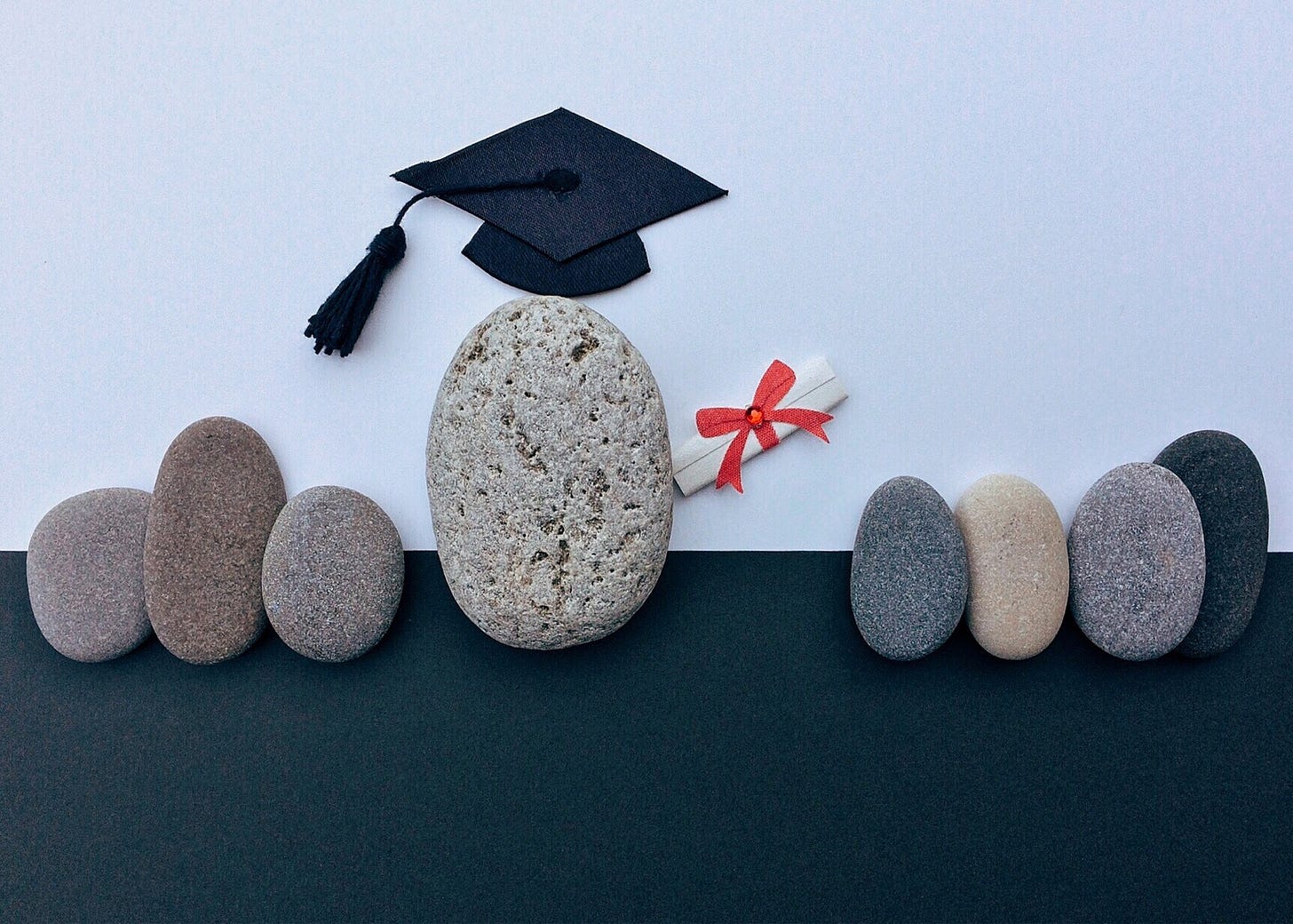 group of 8 small stones, one wearing a mortarboard and carrying a diploma