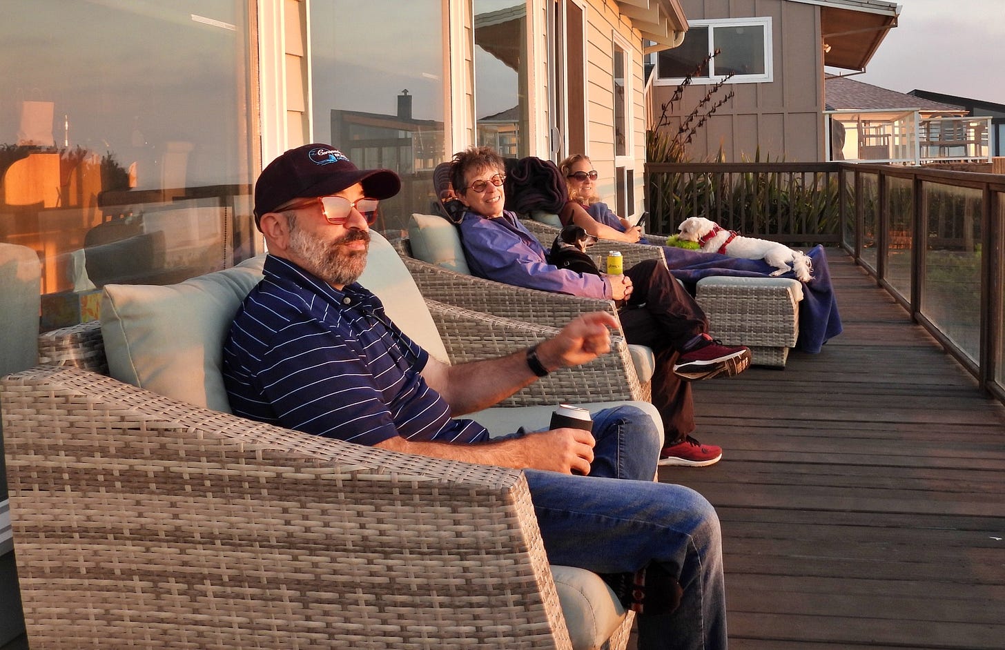 Three people and two dogs sitting on the deck at sunset.