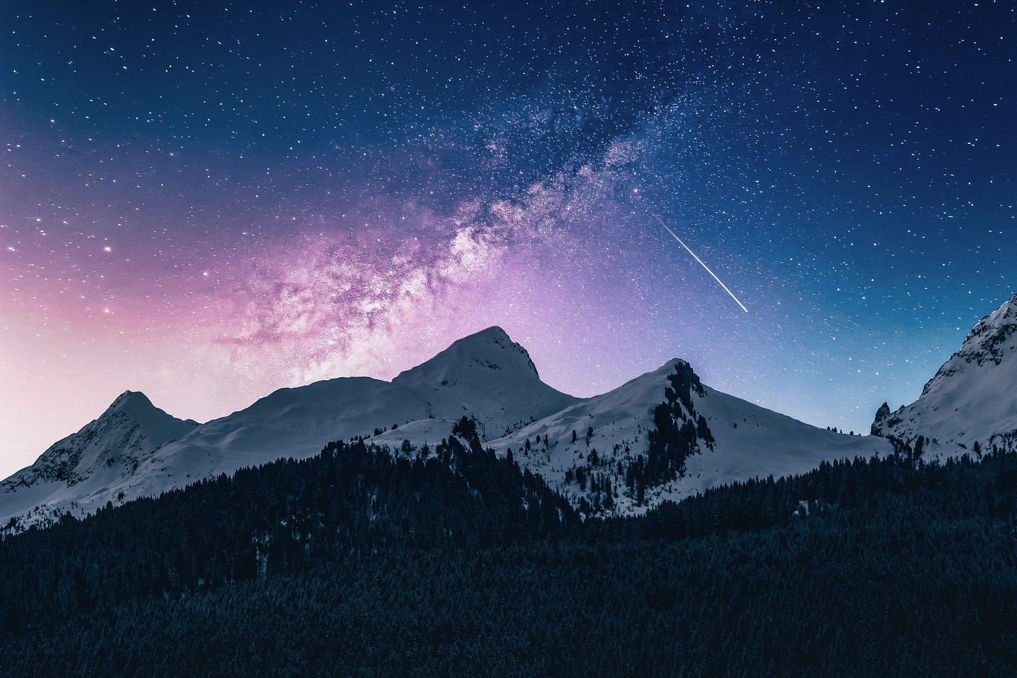 A snowy mountain range, with a forest in the foreground and the night sky behind. The sky is pink fading into blue with the milky way at the centre and a sea of stars.