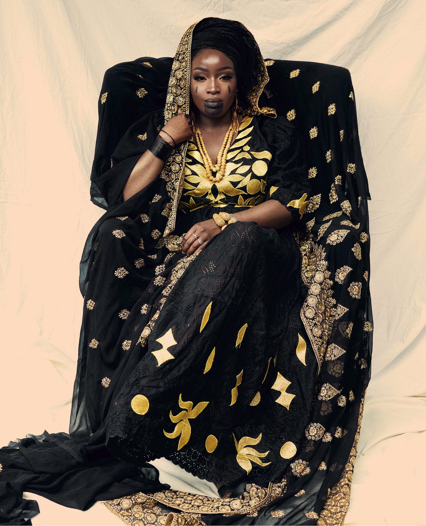Lovette Jallow seated on a chair in traditional Fulani and Wolof regalia, wearing face scarifications. Her posture and dress signify her matriarchal lineage and the weight of the Jallow name—one associated with griot memory, leadership, and ancestral authority in West African tradition. Lovette Jallow seated on a chair in traditional Fulani and Wolof regalia, wearing face scarifications. Her posture and dress signify her matriarchal lineage and the weight of the Jallow name—one associated with griot memory, leadership, and ancestral authority in West African tradition.