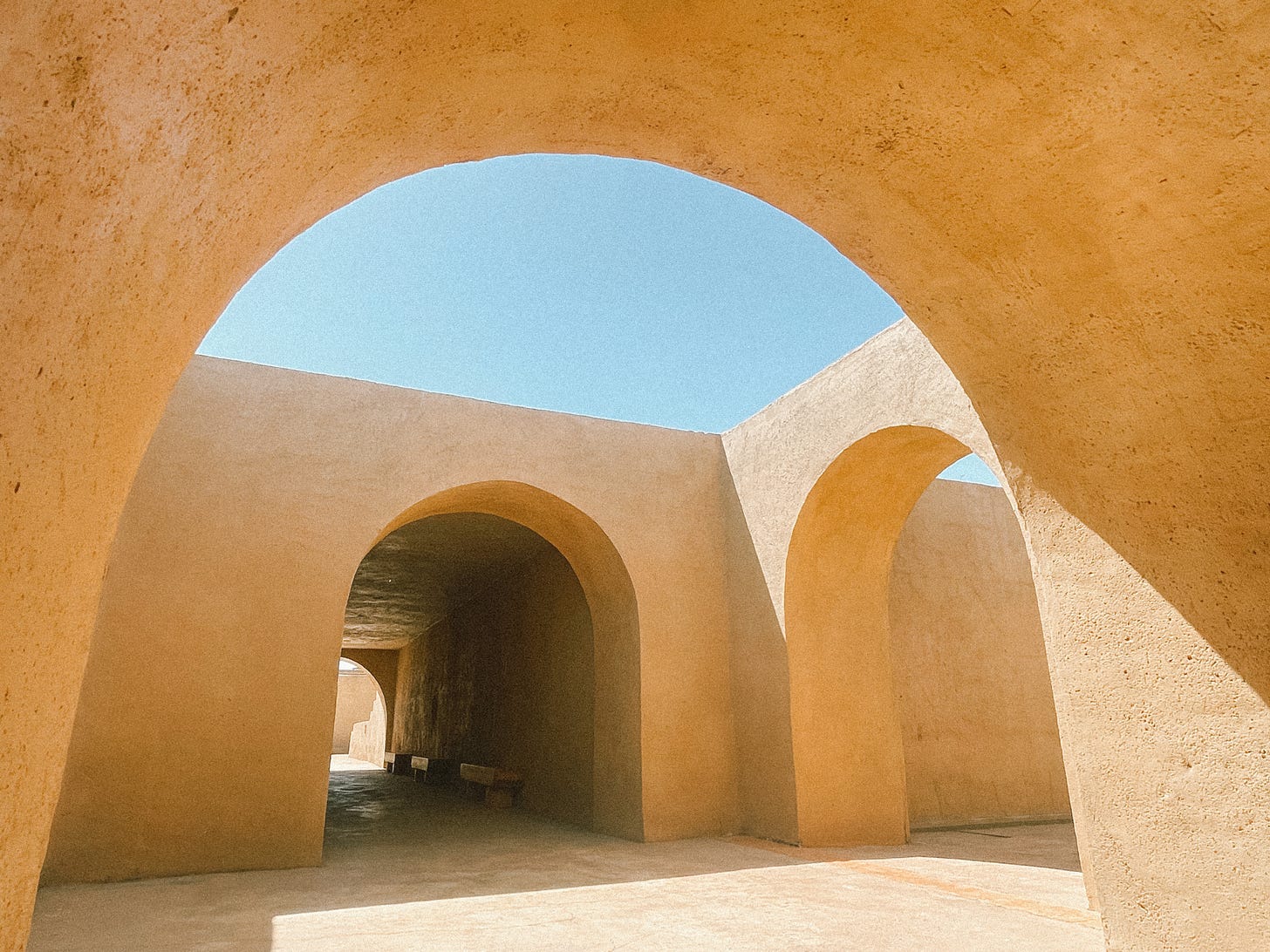 Packed sand and dirt are shaped into archways, creating the earthen walls of a house. A blue sky sits above
