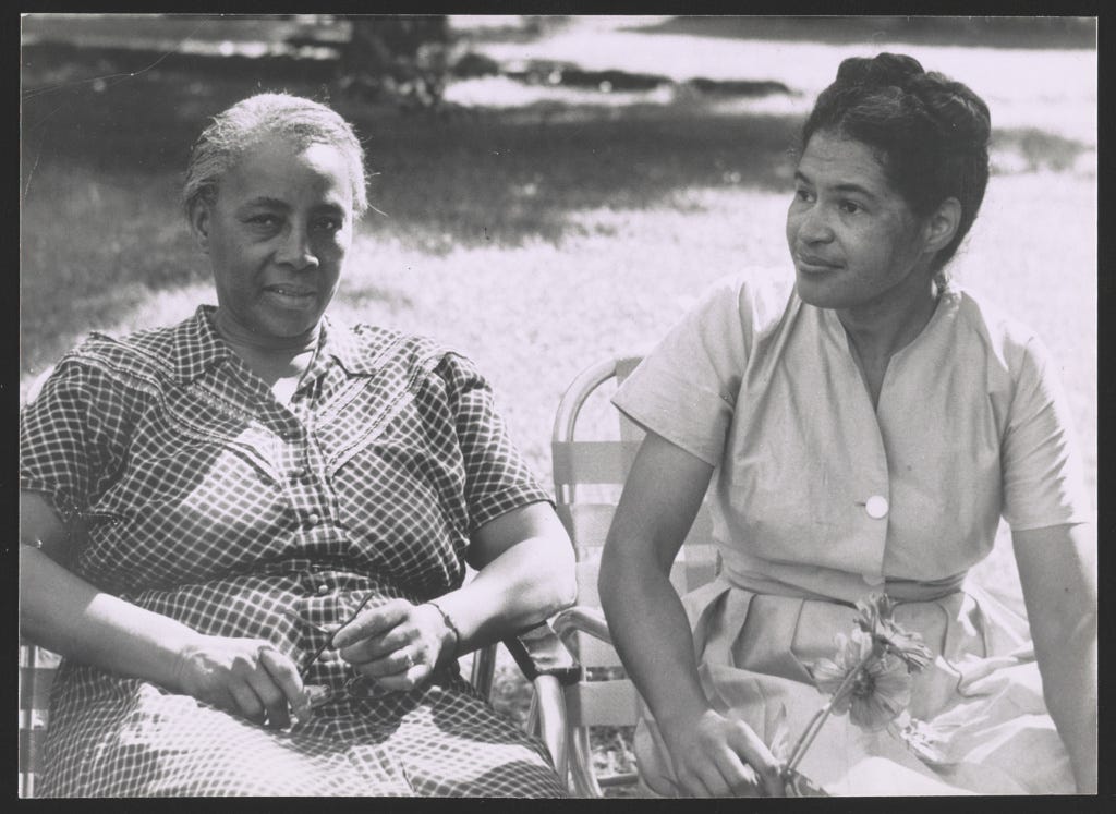 Two women sitting outdoors on sunny day, older woman on left in dark checked dress, younger woman on right in cream dress.