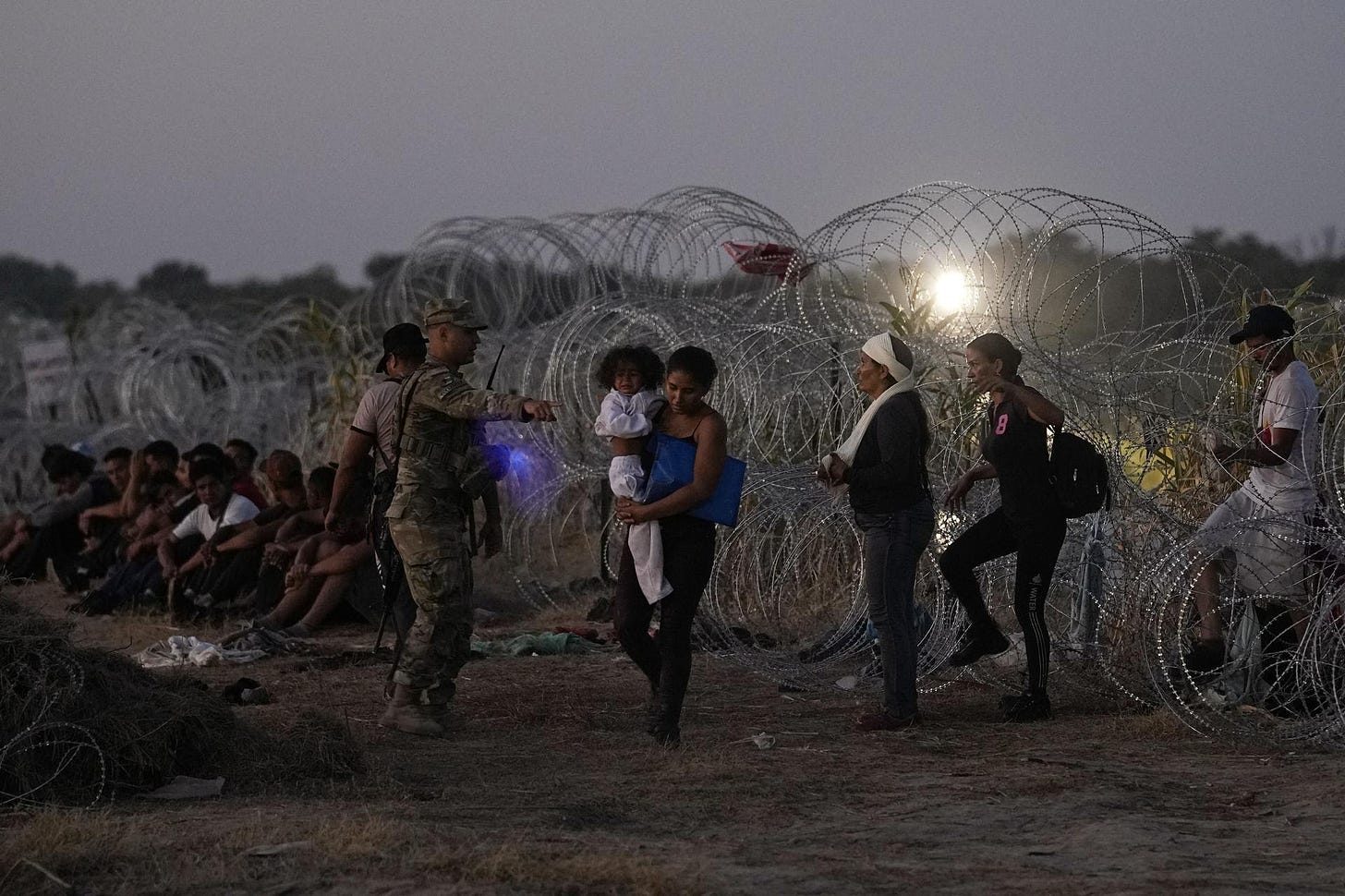 Migrants line up for processing after passing through razor wire.