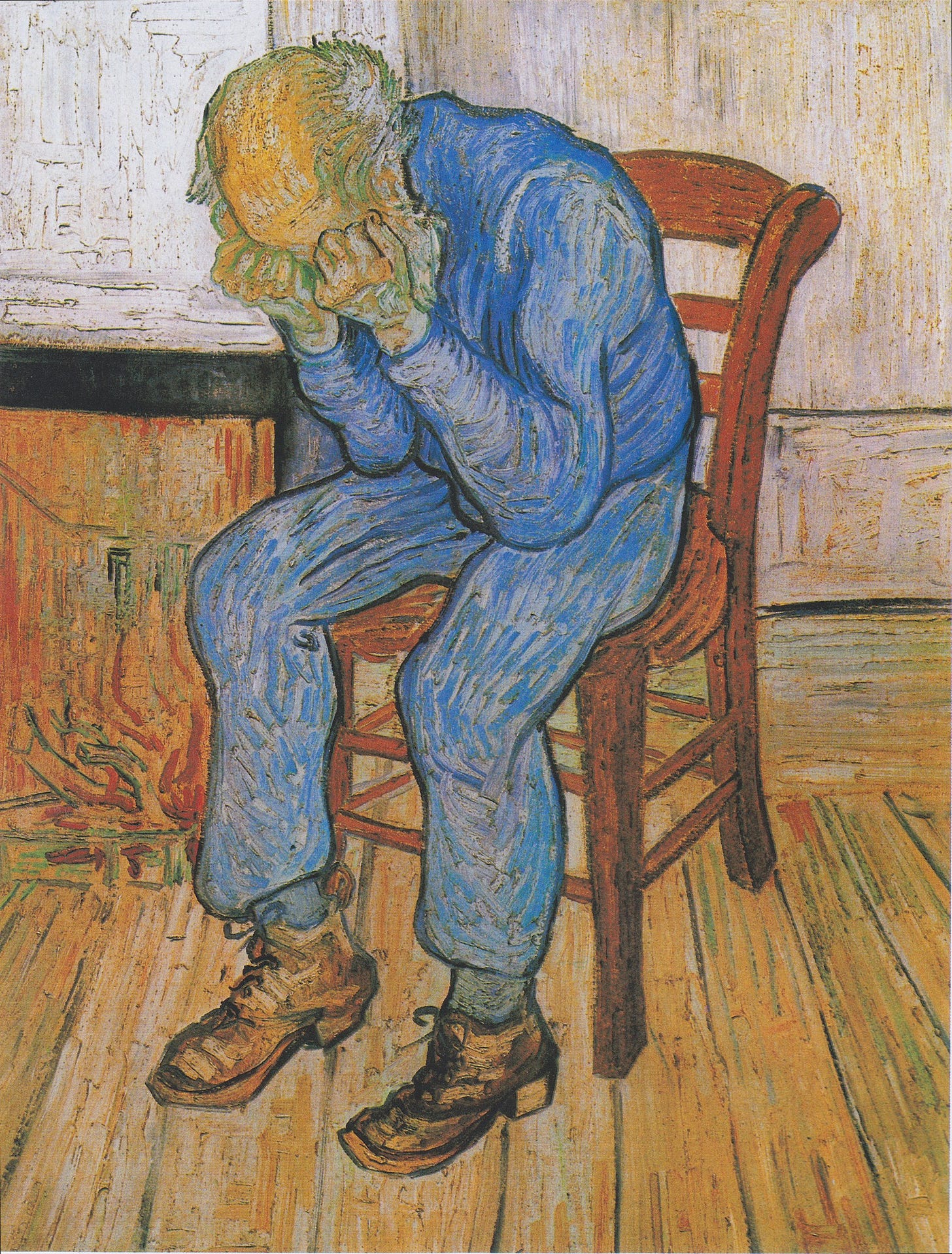 An elderly man with a bald head is sitting on a yellow chair by his fire. There is a low fire in the grate. He is dressed in blue clothes. He is holding his head in his hands.