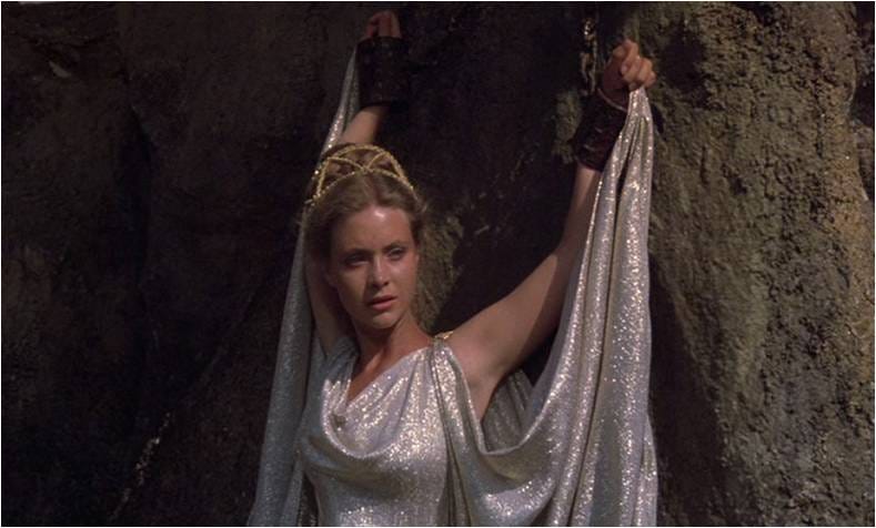 A woman in greek style silver clothes. Chained to a rock hands above her head.