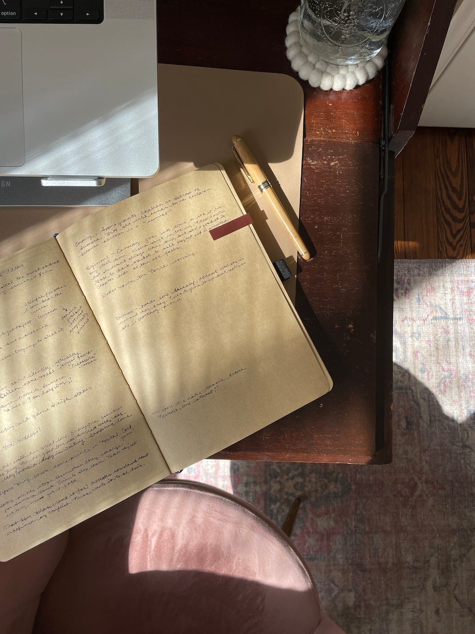A kraft paper notebook sits open on a desk with a laptop keyboard in the corner. There is scribbly cursive in the notebook.