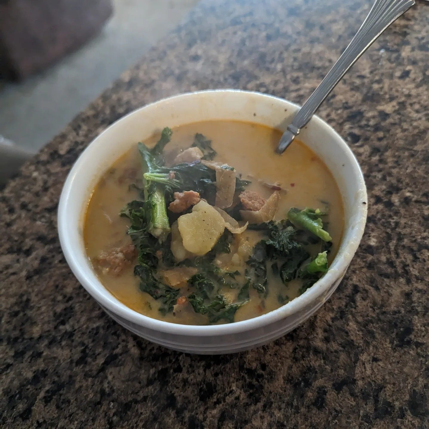 zuppa toscana in a bowl with a spoon sticking out on a kitchen counter