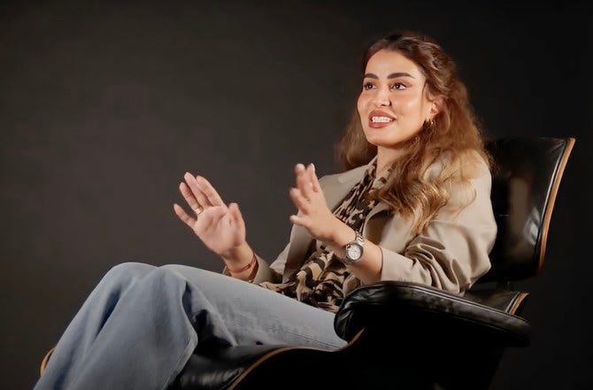 A Saudi woman is speaking and using her hands as she sits in a fancy leather chair.