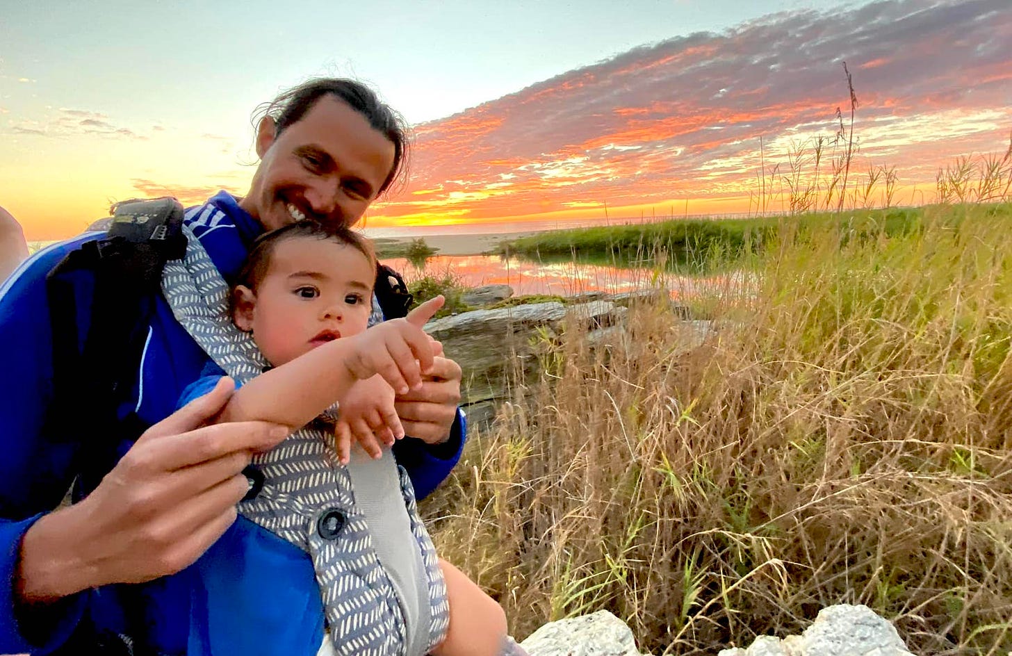 Gino with his very young son smiling against a sunset sky