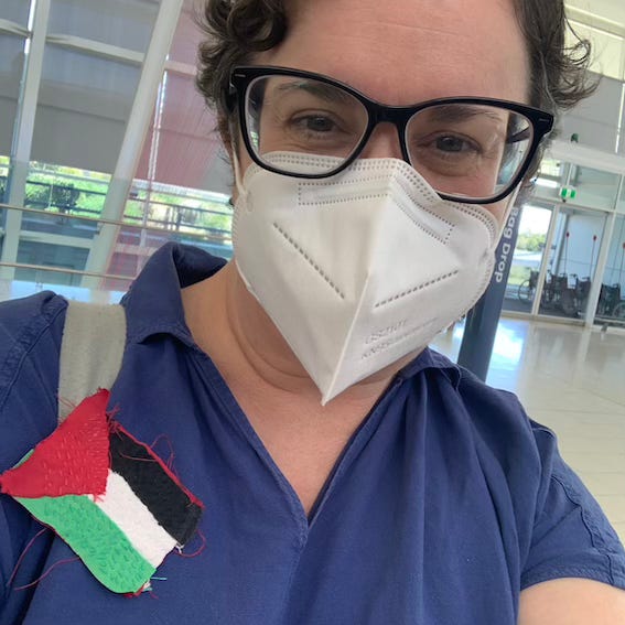 Kate at an airport wearing a mask and Palestine flag badge