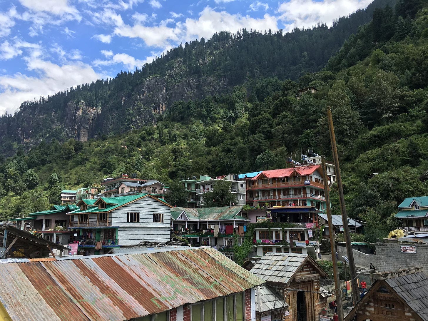 View from a rooftop overlooking tin roofting and buildings made of wood. A mountain, with evergreen trees covering it, is seen in the distance.