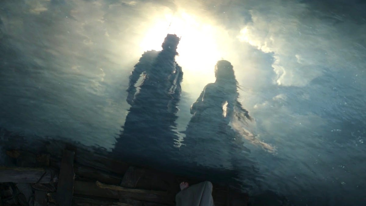 Sauron and Galadriel stand side by side in a reflection in the water surrounding the raft where Galadriel and Halbrand met