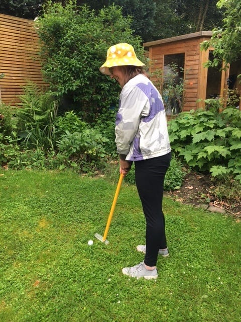 Jane in her garden in a golf stance using a yellow Neowalk stick as a golf club