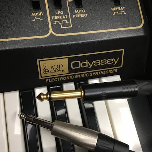 Close up of ARP Odyssey synthesizer with two audio plugs and cables. 