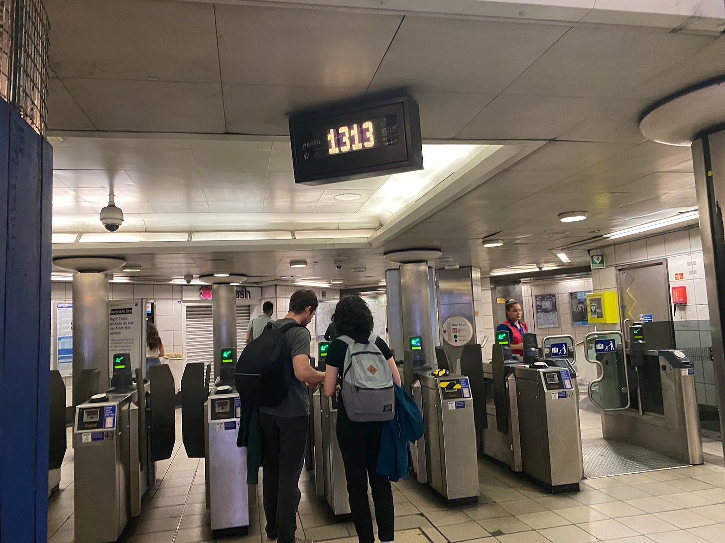 People going through a turnstile in the MTR. A clock reads 1313