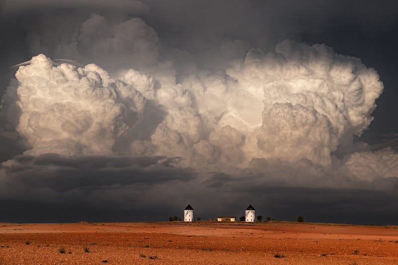 una gran nube tormentosa se forma sobre La Mancha, el suelo está anaranjado y se ven dos molinos blancos