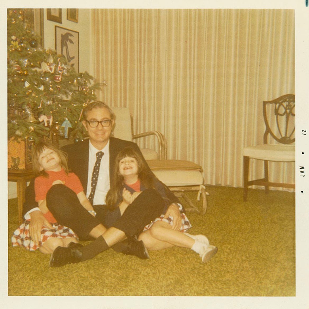 father and two young daughters in front of christmas tree