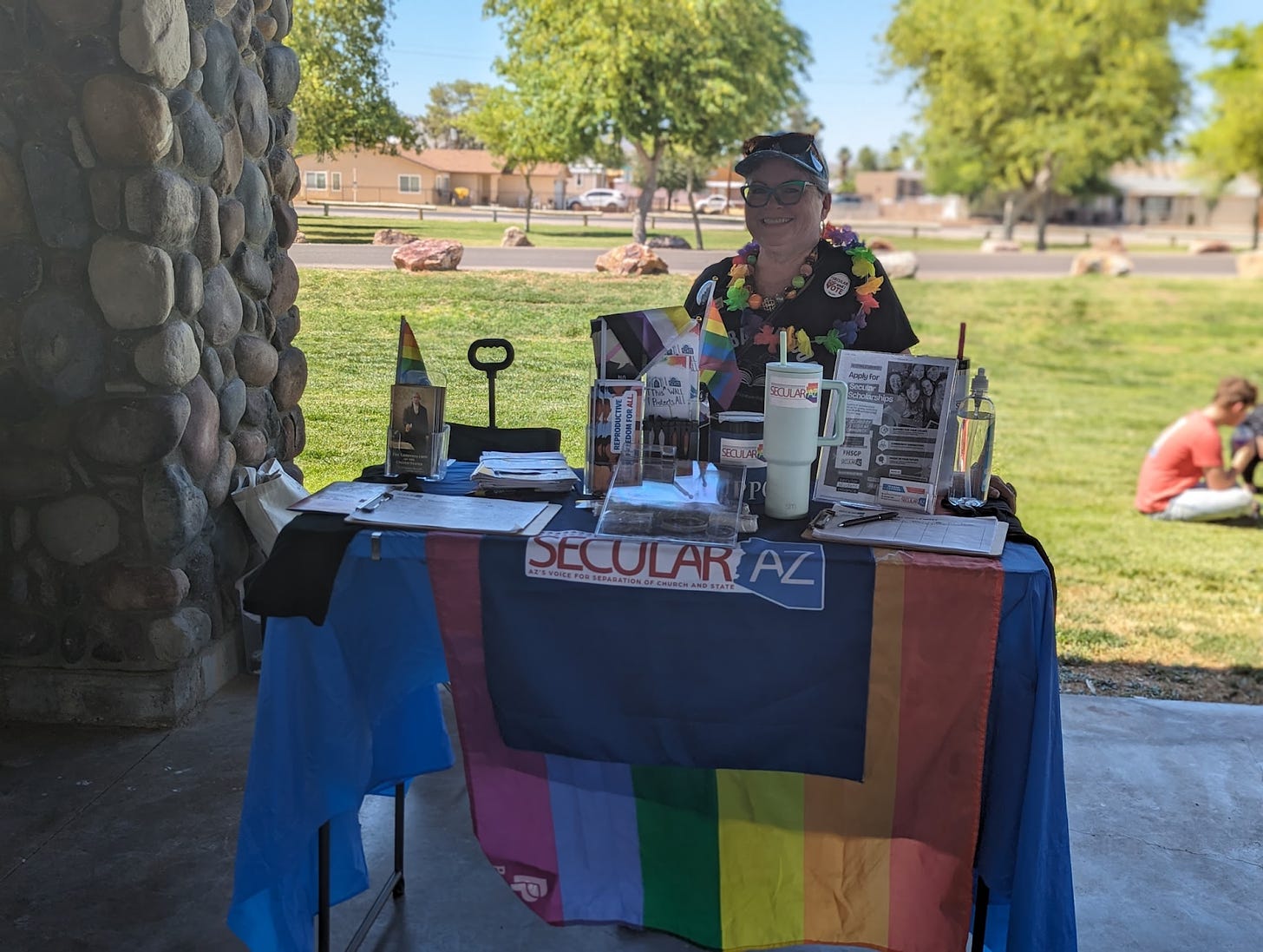 Photo of Karen McClellan at the Secular AZ Table, bedecked in rainbows, at Bisbee Pride