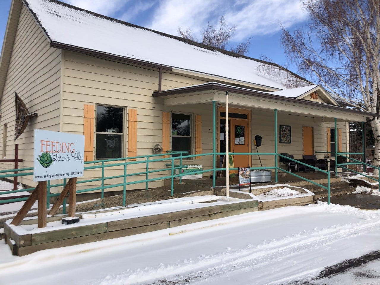 Beige building with orange trim and green railings is covered with snow on an early spring day. A sign reads "Feeding Laramie Valley"