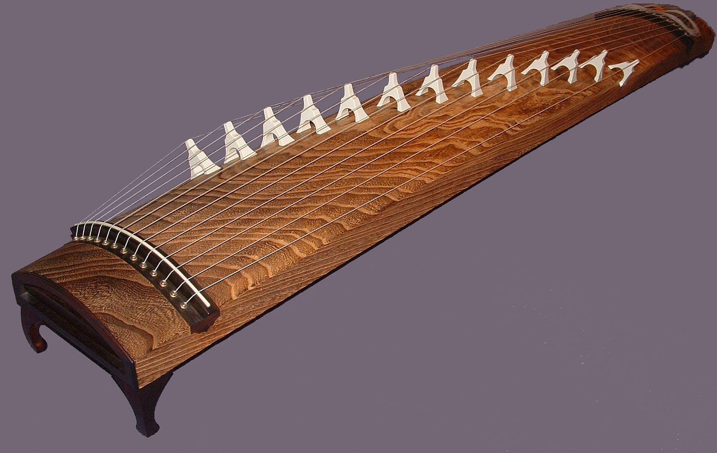 A long, rectangular wood instrument with a slight horizontal curve, strung along its length with raised strings.