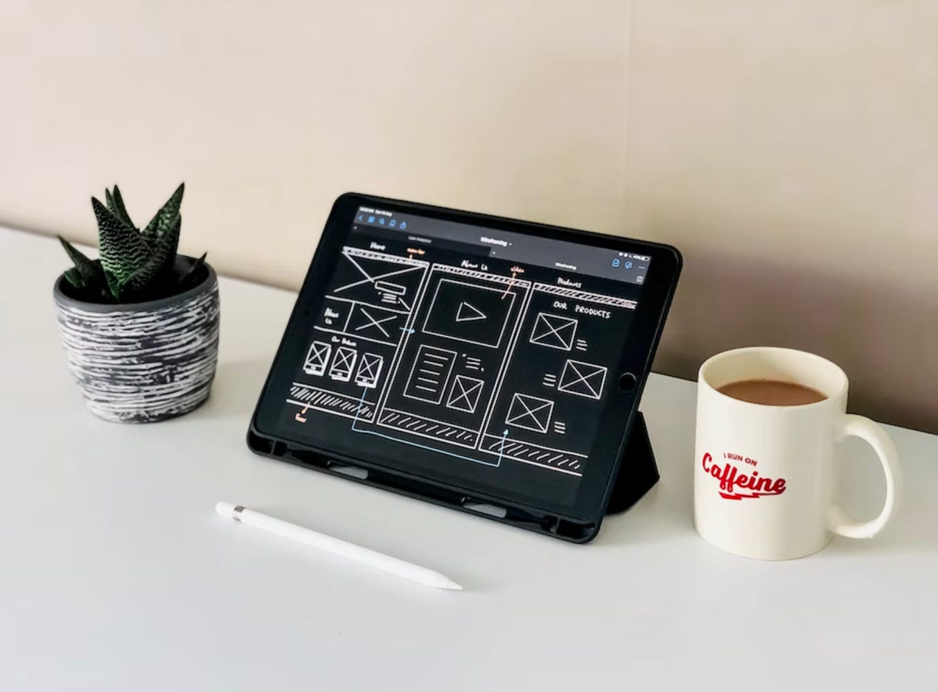 wireframe sketch on a tablet, sitting on a desk next to a cup of coffee and a succulent