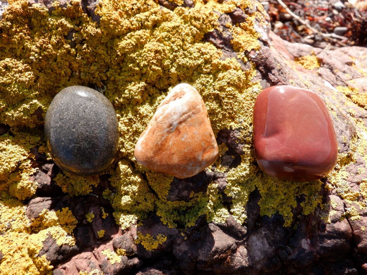 Three pebbles: one round and grey, one triangular and orange, one square and red.