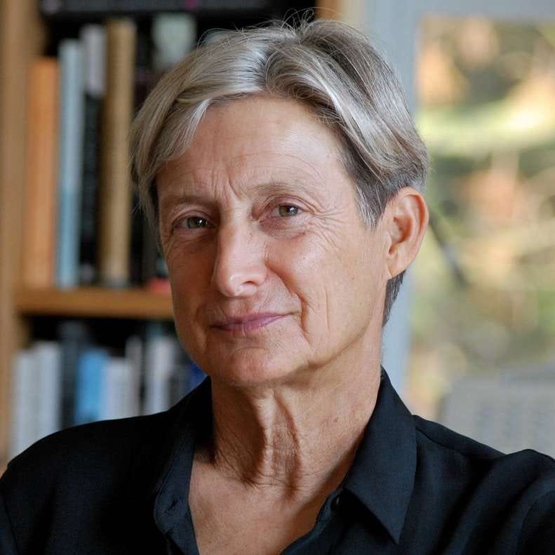 Judith Butler, wearing a black shirt and with gray hair, looks confidently at the camera.