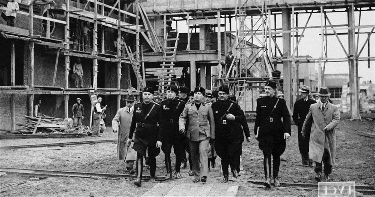 Italian fascist leader Benito Mussolini walking through the Cinecitta studio in Rome with a group of officials and men in uniform