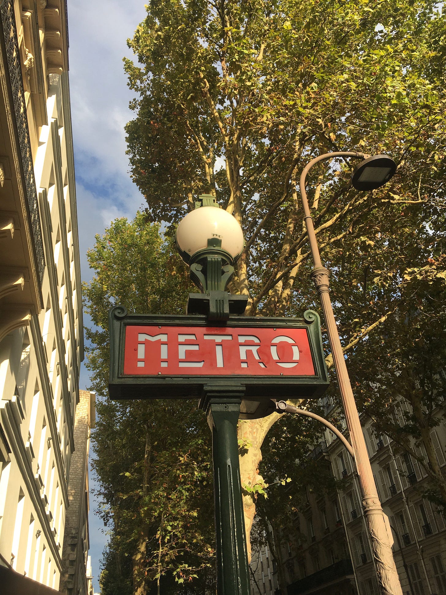 ein rot-grünes Pariser Metro-Schild mit einer Hausfassade und einem Baum im Hintergrund.