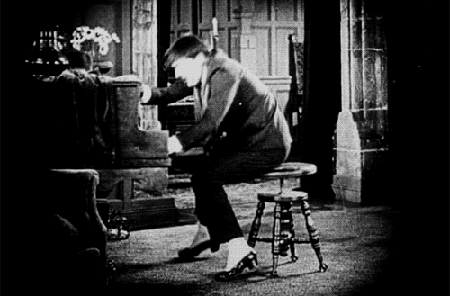 A black and white gif of a man playing the piano and then swinging around on a chair