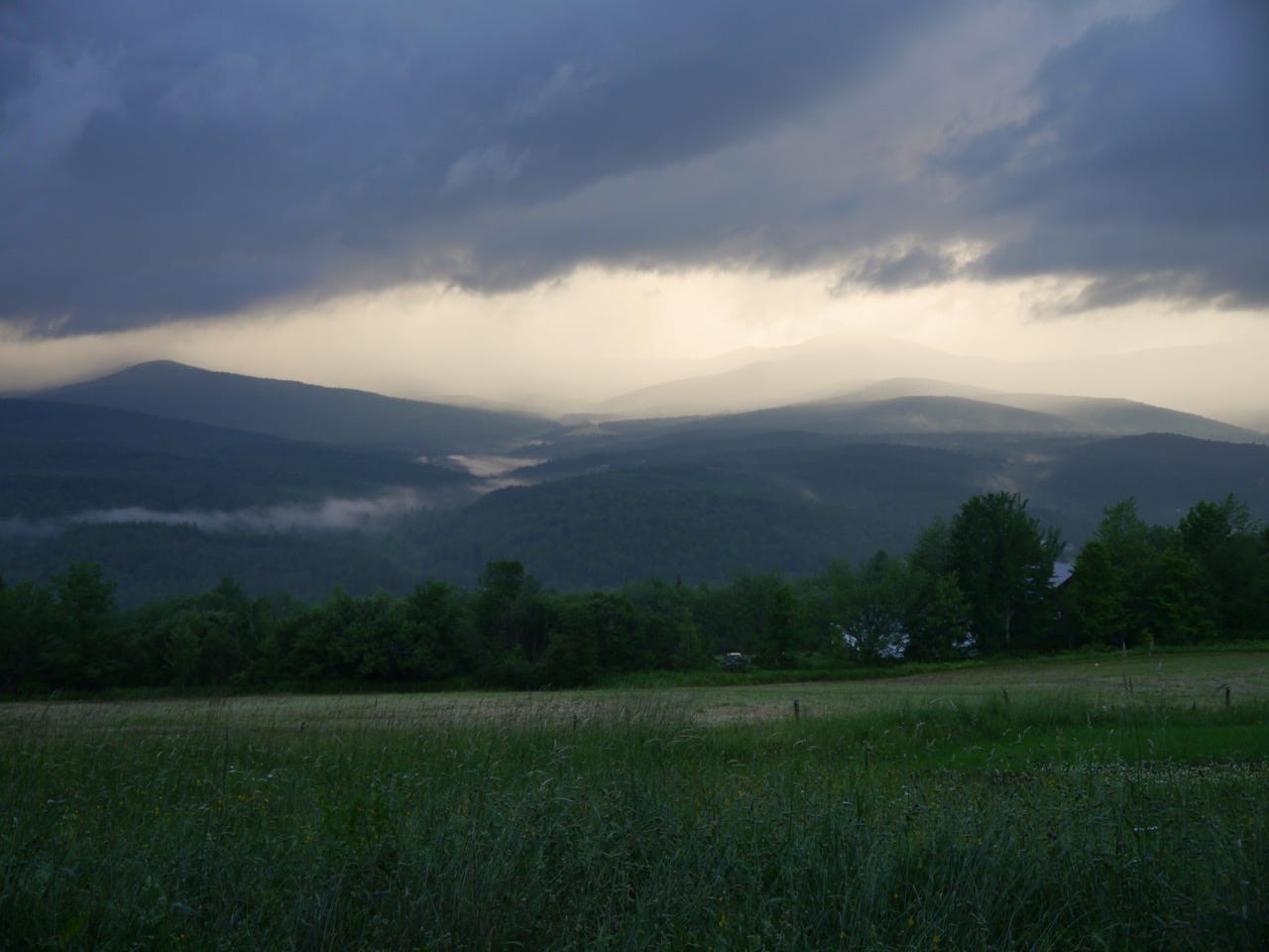 A field and mountains with layers of fog and clouds