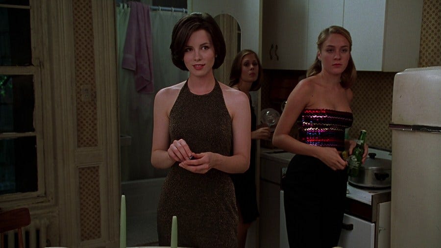 Three white women standing in a New York City apartment in outfits preparing to go a club