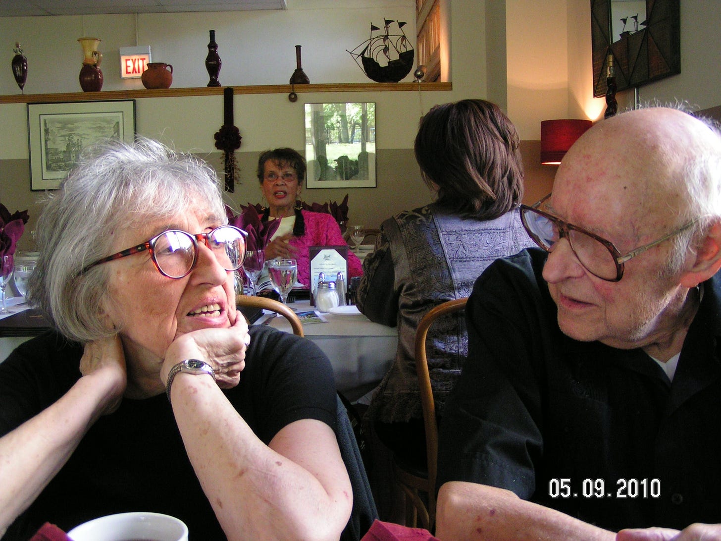 An elderly woman (my mom, Bunny Selden) and man (my late stepfather, Frank Rosen) chatting at a table in a restaurant. In the bottom right-hand corner, there is an imprinted date showing the photo is from May 9, 2010.