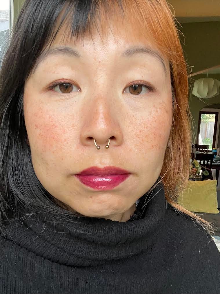 Jane C. Hu is an asian woman with black and red hair, a nose ring and freckles. She's wearing bright berry lipstick