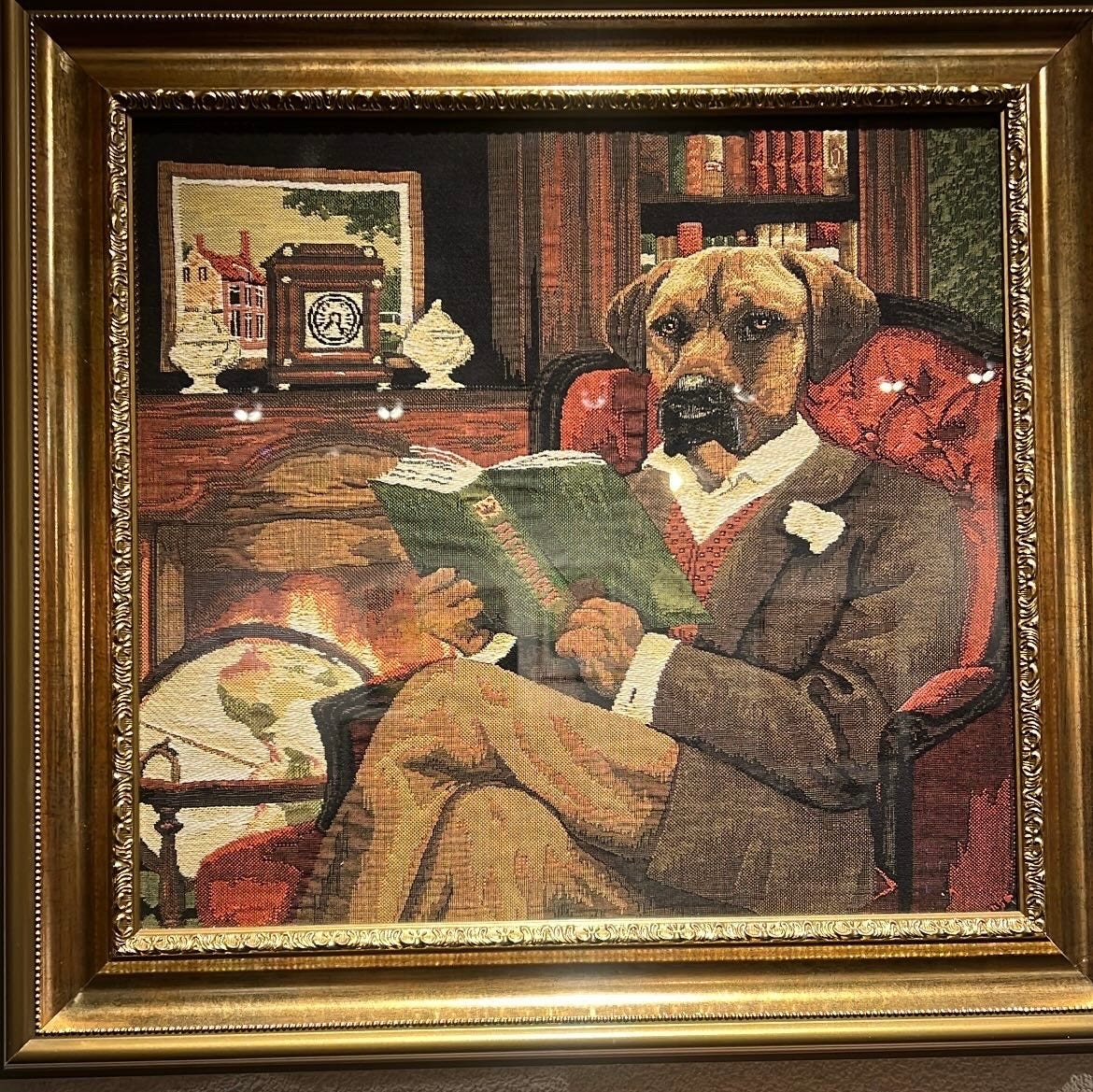 Foto de um quadro de tapaeçaria que mostra um cão todo trajado de senhor, lendo um livro sentado em uma poltrona. O cachorro parece o meu cão Batista.