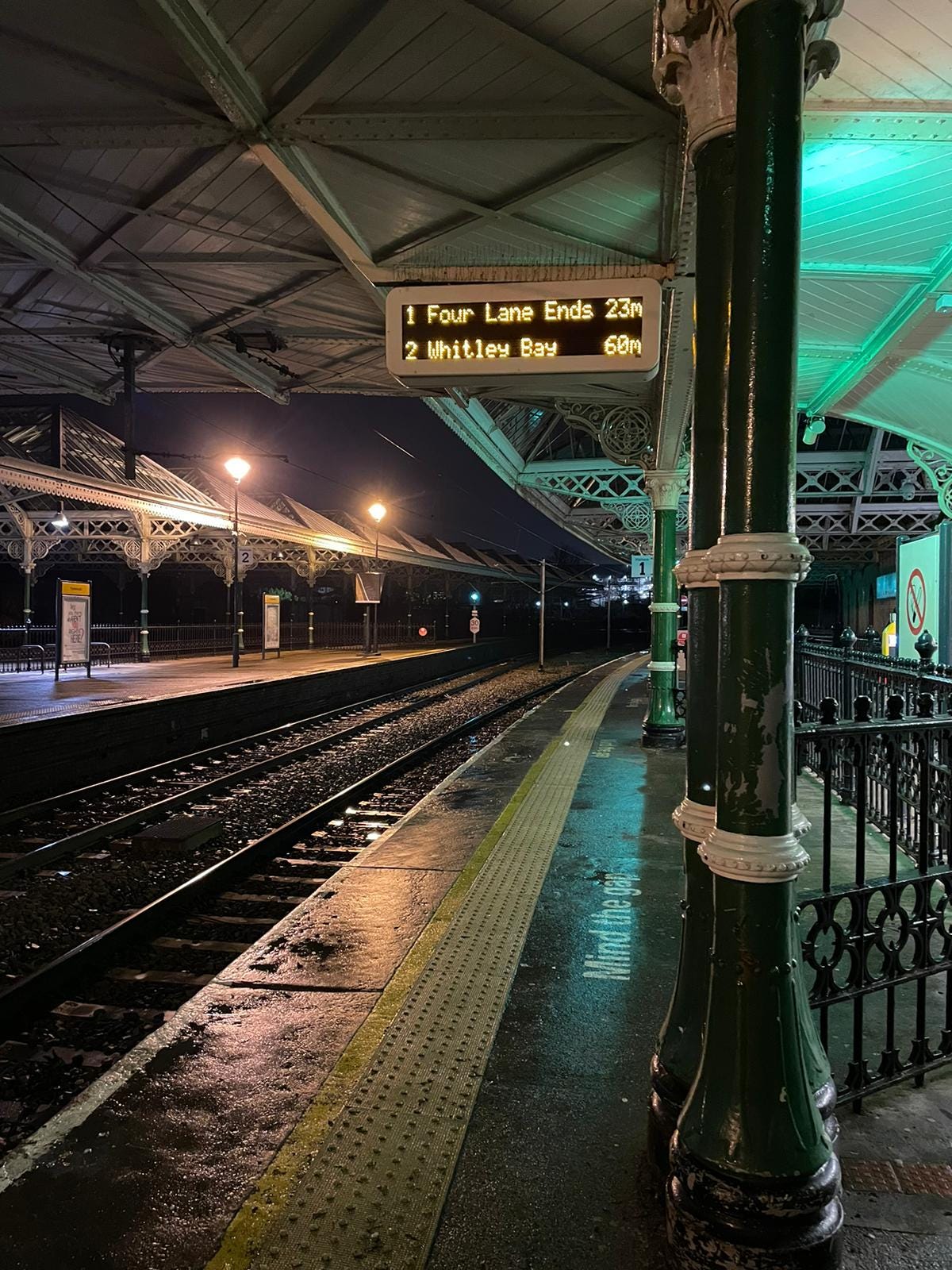 Tynemouth metro station at night. The times on the board read "Four Lane Ends, 23m; Whitley Bay, 60m"