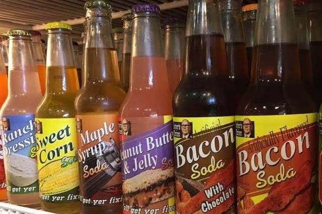 A row of soda bottles in the following flavors, left to right: ranch dressing, sweet corn, maple syrup, peanut butter & jelly, bacon with chocolate, bacon