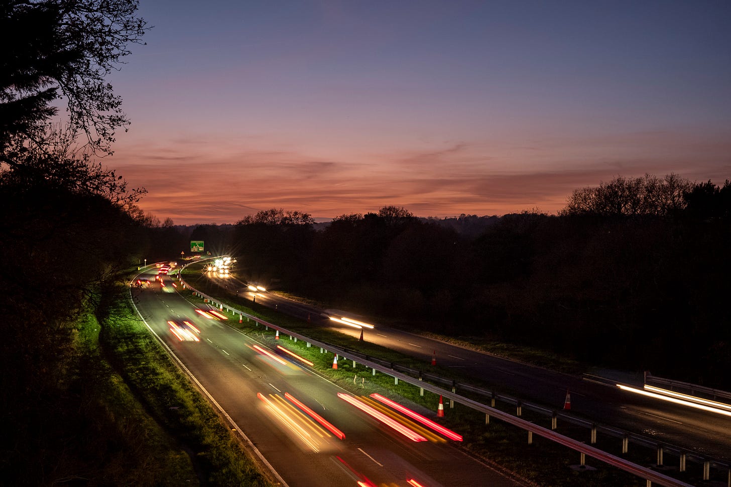 A road at dusk with long, blurred red tail lights and white headlights of cars
