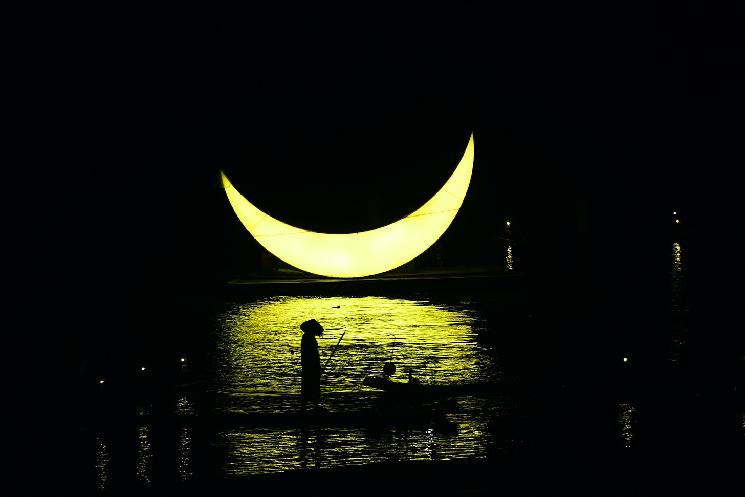 Sullo sfondo, una mezzaluna illuminata di giallo (è un oggetto di scena); in primo piano, due uomini su una zattera. Uno indossa un cappello. La luce è gialla.