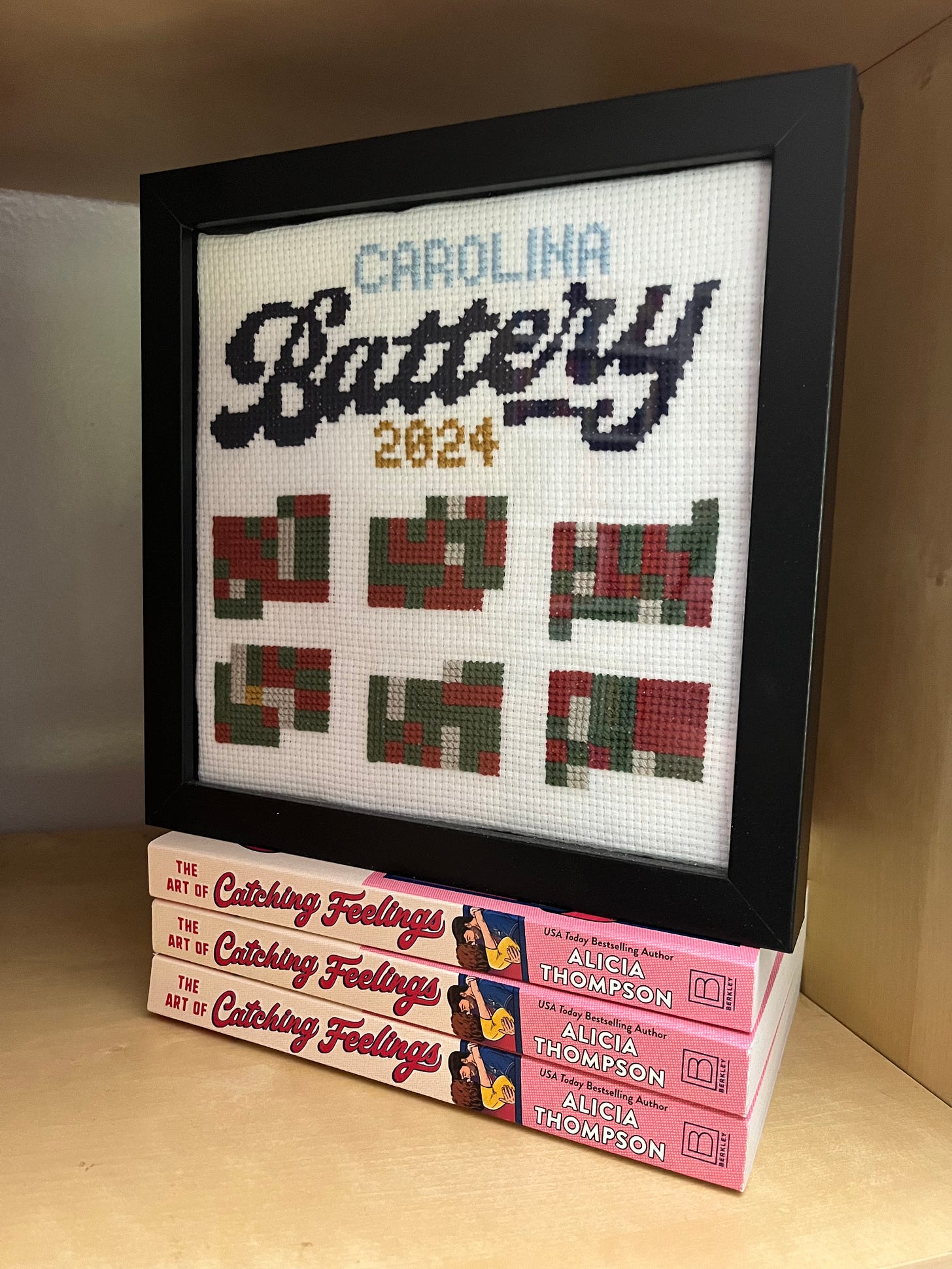 A photo of a cross-stitch baseball calendar showing different color squares for away games, home games, off days, etc., with Carolina Battery 2024 at the top)