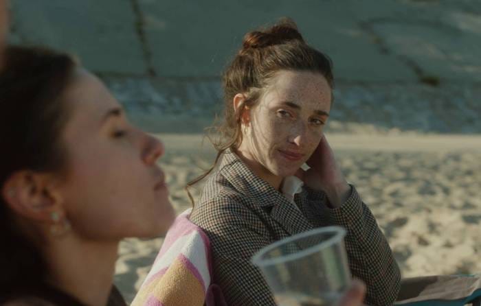 A freckled femme, in focus, looks at her sister, blurry.