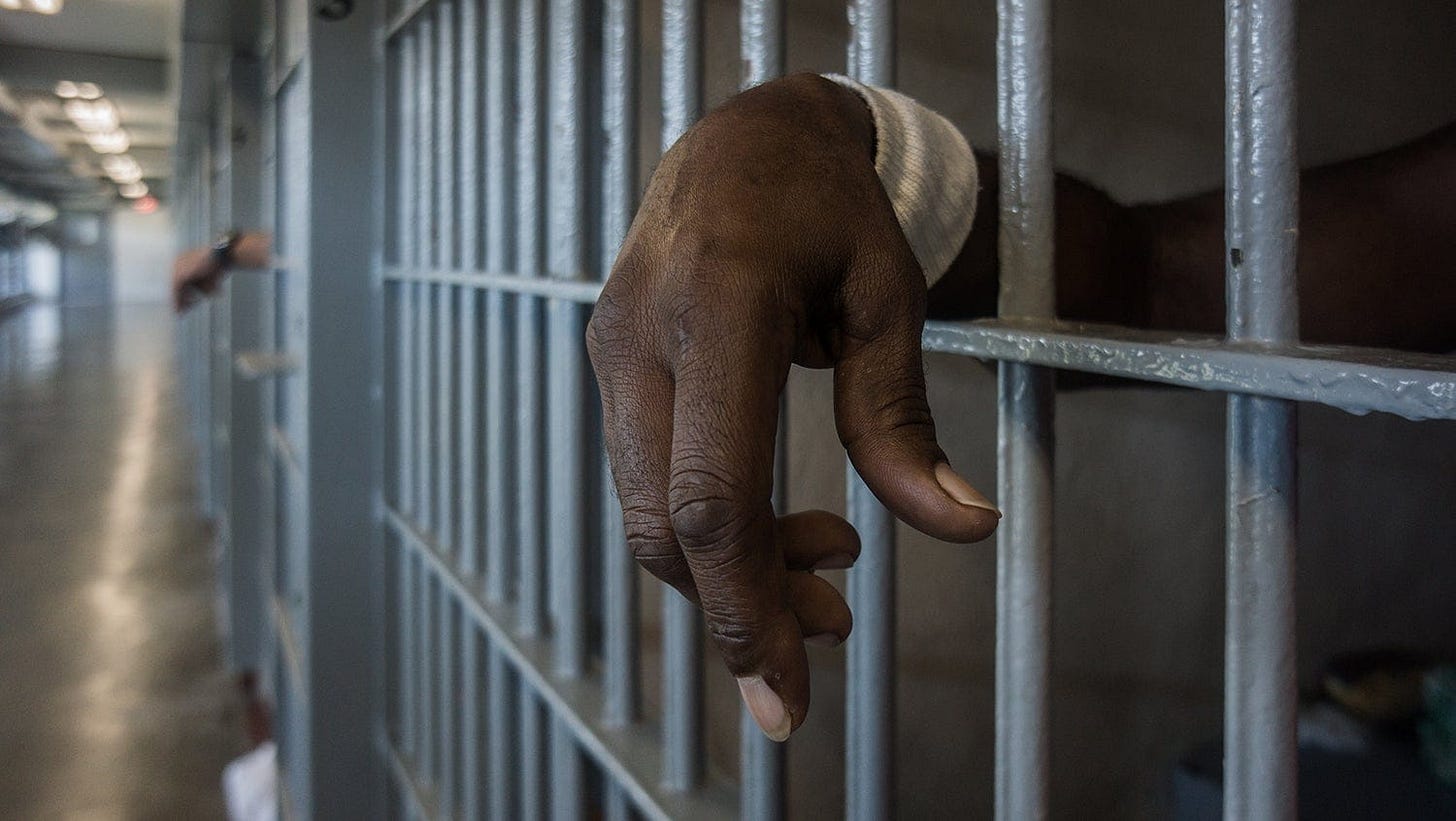 A Black inmate's hand extends out of a prison cell