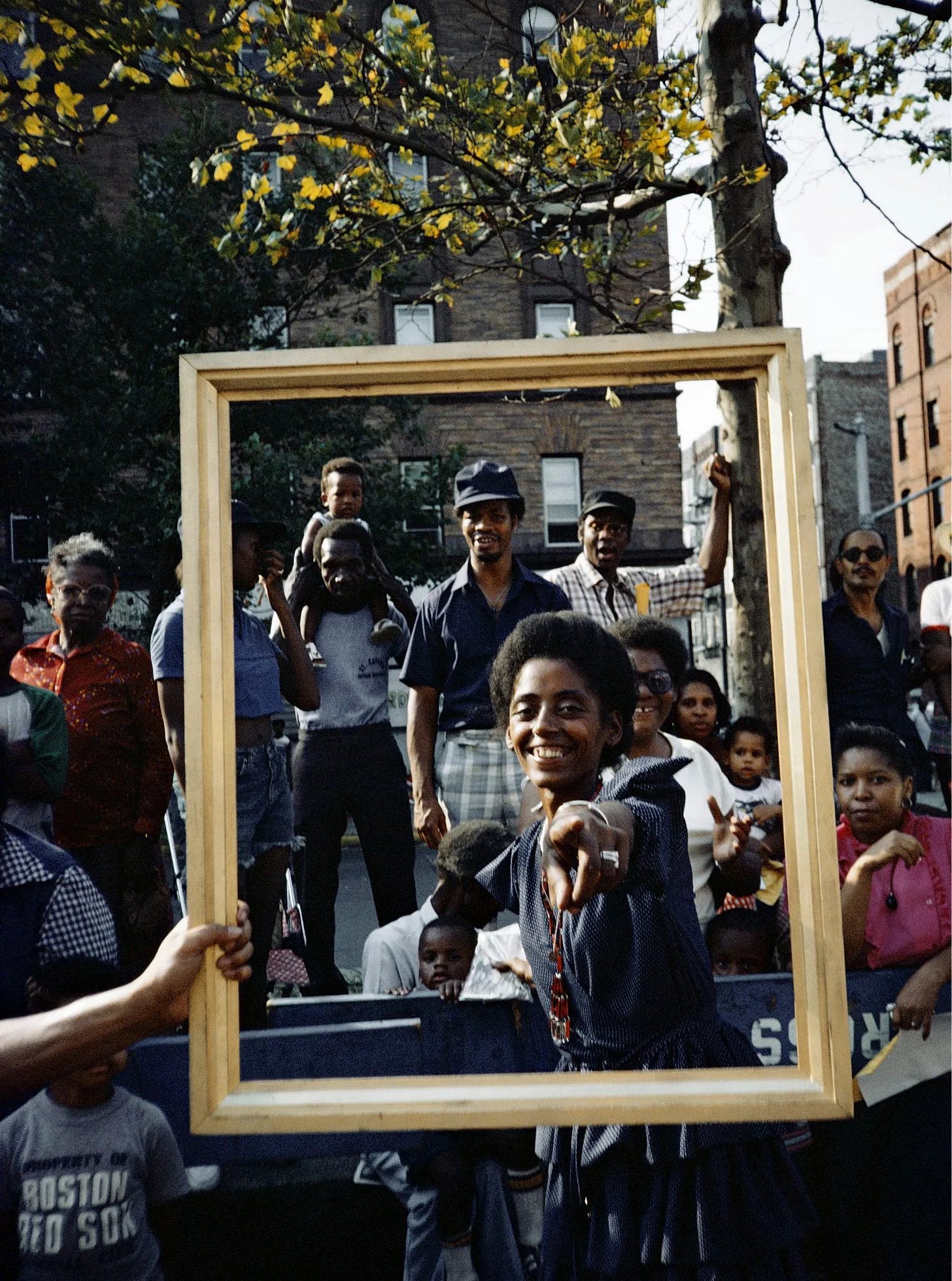 Golden framing of black men, women and children. This is a black woman pointing to the camera and smiling in the center of the frame.