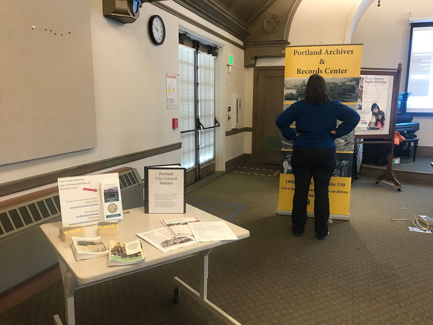 Brochures and handouts on a table and a person standing in front of a sign with 4 images