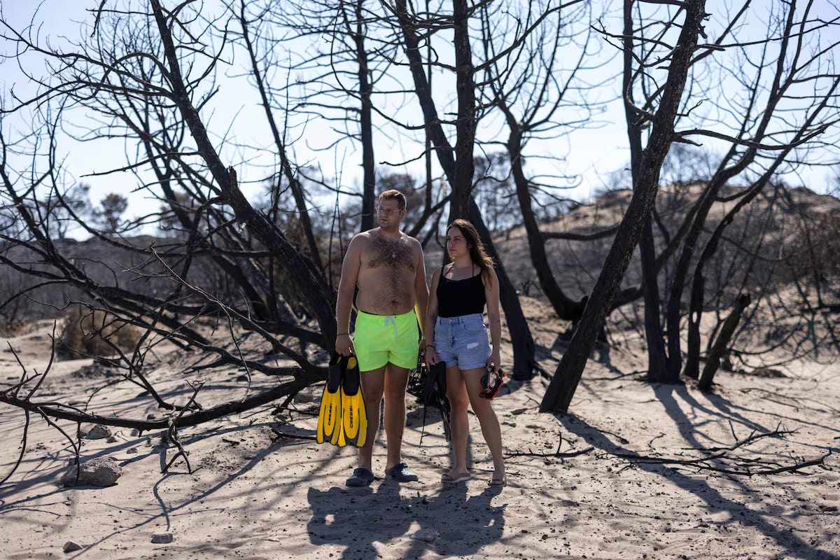 Nickolas Balgouranidis and his wife, Eleni Kottorou, stand under the relative shade of a burnt tree on Glistra Beach on July 28, 2023, in Lardos, Rhodes, Greece. The couple, who are from mainland Greece, were working at Mitsis Faliraki Beach Hotel before everyone was evacuated during the wildfires and are now out of work. Photo: Dan Kitwood/Getty Images.