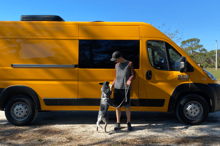 Scout the blue heeler stands on her hind legs against her owner in front of a bright yellow custom campervan conversion